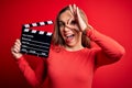 Young beautiful blonde clapper woman holding clapboard over isolated red background with happy face smiling doing ok sign with Royalty Free Stock Photo