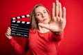 Young beautiful blonde clapper woman holding clapboard over isolated red background with open hand doing stop sign with serious Royalty Free Stock Photo