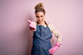 Young beautiful blonde cleaner woman doing housework wearing arpon and gloves smiling friendly offering handshake as greeting and Royalty Free Stock Photo