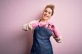 Young beautiful blonde cleaner woman doing housework wearing arpon and gloves smiling in love doing heart symbol shape with hands