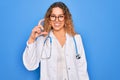 Young beautiful blonde doctor woman with blue eyes wearing coat and stethoscope smiling and confident gesturing with hand doing Royalty Free Stock Photo