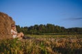 Young beautiful blonde farmer woman in white outfit, sunglasses cowboy hat and boots posing at sunset in field with Royalty Free Stock Photo