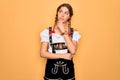 Young beautiful blonde german woman with blue eyes wearing traditional octoberfest dress with hand on chin thinking about