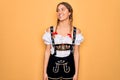 Young beautiful blonde german woman with blue eyes wearing traditional octoberfest dress looking away to side with smile on face, Royalty Free Stock Photo