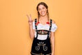 Young beautiful blonde german woman with blue eyes wearing traditional octoberfest dress smiling looking to the camera showing Royalty Free Stock Photo