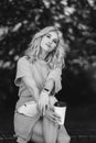 Young beautiful blonde girl in a blue short dress and with a white belt bag walks in a green park. He sits on a bench Royalty Free Stock Photo