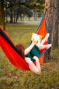 Young blonde girl in hammock reading book. Pretty woman leisure lifestyle at nature ountdoor. Female relax in forest. Royalty Free Stock Photo