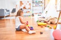 Young beautiful blonde girl kid enjoying play school with toys at kindergarten, smiling happy playing with inteligence toys at