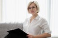 Young beautiful blonde girl with short hair in a white shirt is sitting on the sofa in bright in the office against the Royalty Free Stock Photo