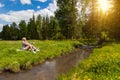 Young beautiful blonde girl in shorts with beautiful legs sits on the banks of a stream and relaxes while listening to the murmur