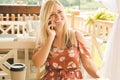 Young beautiful blonde girl in the summer in a cafe drinks coffee, talks on the phone and laughs Royalty Free Stock Photo