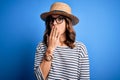 Young beautiful blonde girl wearing glasses and hat over blue  background cover mouth with hand shocked with shame for Royalty Free Stock Photo