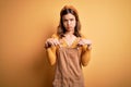 Young beautiful blonde girl wearing overall standing over yellow  background Pointing down looking sad and upset, Royalty Free Stock Photo