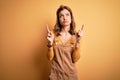 Young beautiful blonde girl wearing overall standing over yellow isolated background Pointing up looking sad and upset, indicating Royalty Free Stock Photo