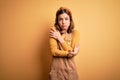 Young beautiful blonde girl wearing overall standing over yellow isolated background shaking and freezing for winter cold with sad Royalty Free Stock Photo