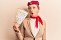 Young beautiful blonde girl wearing stewardess uniform holding boarding pass scared and amazed with open mouth for surprise,