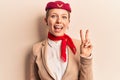 Young beautiful blonde girl wearing stewardess uniform smiling with happy face winking at the camera doing victory sign Royalty Free Stock Photo