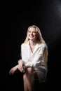 Young beautiful blonde girl in white shirt posing on black background. Adult woman model posing alone in dark studio