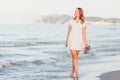 Young beautiful blonde hair curvy model walking on the beach barefooted with flip flops in her hand Royalty Free Stock Photo