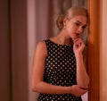 Young beautiful blonde with hair gathered in a chignon in a polka-dot dress stands at the door with  a thoughtful look Royalty Free Stock Photo