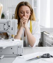 Young beautiful blonde hair seamstress sits at work and shows a headache