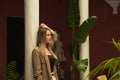 Young and beautiful blonde Latin woman is leaning against a marble column in the inner courtyard of a hotel. The woman is sad and