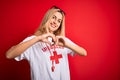 Young beautiful blonde lifeguard woman wearing t-shirt with red cross using whistle smiling in love showing heart symbol and shape