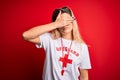 Young beautiful blonde lifeguard woman wearing t-shirt with red cross and whistle covering eyes with hand, looking serious and sad