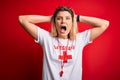 Young beautiful blonde lifeguard woman wearing t-shirt with red cross and whistle Crazy and scared with hands on head, afraid and