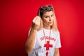 Young beautiful blonde lifeguard woman wearing t-shirt with red cross and whistle Doing Italian gesture with hand and fingers