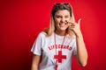 Young beautiful blonde lifeguard woman wearing t-shirt with red cross and whistle Pointing with hand finger to face and nose,
