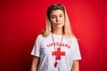 Young beautiful blonde lifeguard woman wearing t-shirt with red cross and whistle Relaxed with serious expression on face