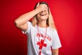 Young beautiful blonde lifeguard woman wearing t-shirt with red cross and whistle smiling and laughing with hand on face covering