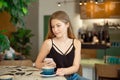 Young beautiful blonde with long hair in a charm top and jeans drinks coffee and looks out the window. Royalty Free Stock Photo