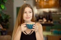 Young beautiful blonde with long hair in a charm top and jeans drinks coffee and looks out the window. Royalty Free Stock Photo