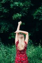 Young beautiful blonde long haired woman in red dress standing backwards with raised hands outdoor. Copy space Royalty Free Stock Photo