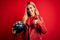 Young beautiful blonde motorcyclist woman holding moto helmet over isolated red background happy with big smile doing ok sign, Royalty Free Stock Photo