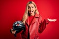 Young beautiful blonde motorcyclist woman holding moto helmet over  red background very happy and excited, winner Royalty Free Stock Photo