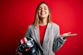 Young beautiful blonde motorcyclist woman holding motorcycle helmet over red background very happy and excited, winner expression Royalty Free Stock Photo