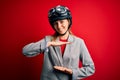 Young beautiful blonde motorcyclist woman wearing motorcycle helmet over red background gesturing with hands showing big and large Royalty Free Stock Photo