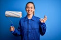 Young beautiful blonde painter woman with blue eyes painting wearing uniform using roller doing ok sign with fingers, excellent Royalty Free Stock Photo