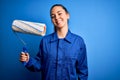 Young beautiful blonde painter woman with blue eyes painting wearing uniform using roller with a happy face standing and smiling Royalty Free Stock Photo