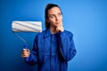 Young beautiful blonde painter woman with blue eyes painting wearing uniform using roller serious face thinking about question, Royalty Free Stock Photo