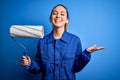 Young beautiful blonde painter woman with blue eyes painting wearing uniform using roller very happy and excited, winner Royalty Free Stock Photo