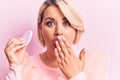 Young beautiful blonde plus size woman applying makeup using sponge over pink background covering mouth with hand, shocked and Royalty Free Stock Photo