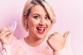 Young beautiful blonde plus size woman applying makeup using sponge over pink background pointing thumb up to the side smiling Royalty Free Stock Photo