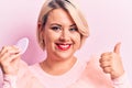 Young beautiful blonde plus size woman applying makeup using sponge over pink background smiling happy and positive, thumb up Royalty Free Stock Photo