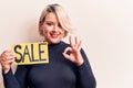 Young beautiful blonde plus size woman holding sale banner over isolated white background doing ok sign with fingers, smiling Royalty Free Stock Photo