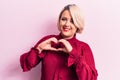 Young beautiful blonde plus size woman wearing casual shirt over isolated pink background smiling in love doing heart symbol shape Royalty Free Stock Photo