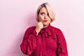 Young beautiful blonde plus size woman wearing casual shirt over isolated pink background thinking concentrated about doubt with Royalty Free Stock Photo